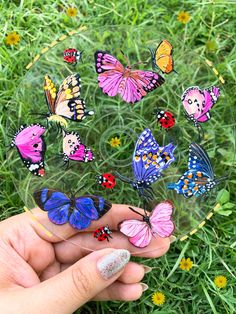 a hand holding a glass plate with many colorful butterflies on it in the middle of some grass