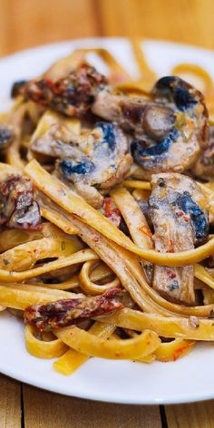 a white plate topped with pasta covered in mushrooms and sauce on top of a wooden table