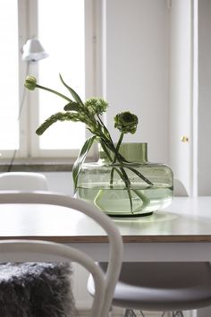 a glass vase with flowers in it sitting on a table next to two white chairs