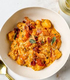 a white bowl filled with food on top of a table next to a glass of wine