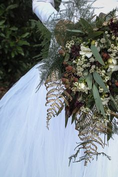 a bride holding a bouquet of flowers and greenery