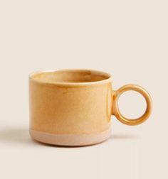 a yellow coffee cup with a ring handle on it's side, against a white background