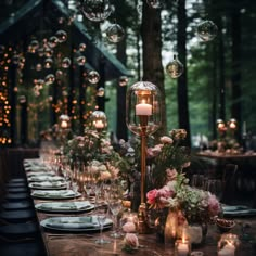 a long table with candles, plates and flowers on it in the middle of a forest