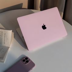 an apple laptop computer sitting on top of a white table next to a purple iphone