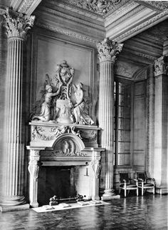 an old black and white photo of a fireplace in a large room with columns, sculptures and chairs