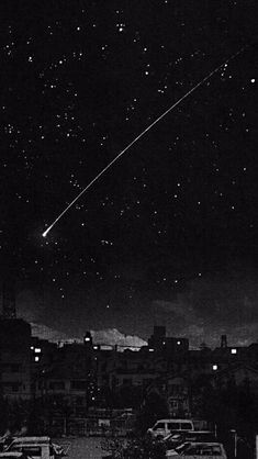 an airplane is flying in the night sky over some buildings and cars parked on the street