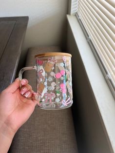 a person holding up a coffee mug in front of a window with blinds on it