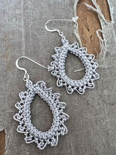 the crocheted hoop earrings are hanging from hooks on a piece of linen fabric