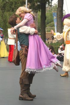 a man and woman in costume hugging each other on the street while people watch from behind them