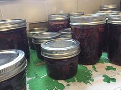 many jars of jam are lined up on a green tablecloth in front of a white tile wall