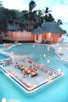 people are sitting at a table in the middle of an outdoor pool with candles on it