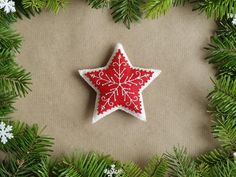 a red and white felt star ornament surrounded by evergreen branches