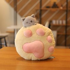 a cat stuffed animal sitting on top of a round cushion with pink paws and feet