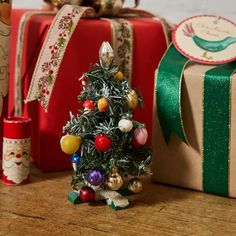 a small christmas tree sitting on top of a wooden table next to presents and wrapping paper