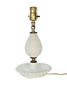 a white table lamp with a gold colored light bulb on the base and beaded glass shade