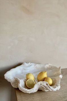 some lemons are in a white bowl on a wooden table next to a wall