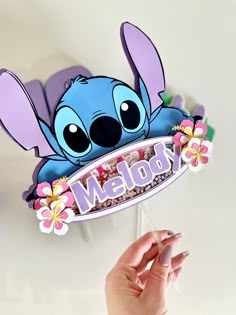 a hand holding up a lollipop sign with stitchy ears and flowers on it