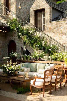 an outdoor seating area with chairs and tables in front of a stone building that has stairs leading up to the second floor