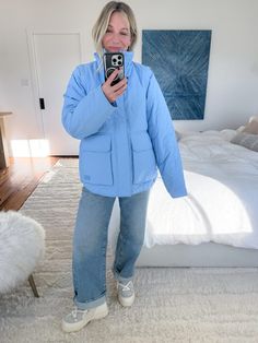 a woman taking a selfie while standing in front of a bed and holding a camera