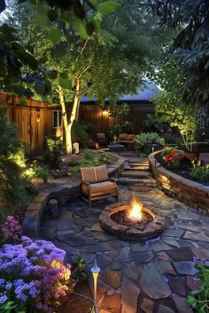 an outdoor fire pit surrounded by flowers and trees in the evening time with lights shining on it