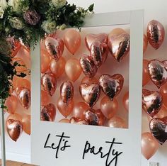 there are balloons in the shape of hearts on this party wall with flowers and greenery