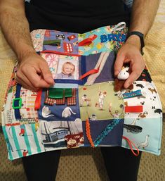 a man sitting on the floor holding a piece of cloth covered in pictures and sewing threads