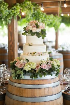 a wedding cake sitting on top of a wooden barrel next to wine glasses and flowers