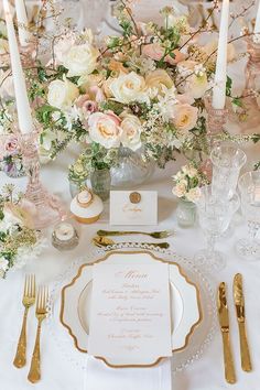 the table is set with white and gold plates, silverware, and pink flowers