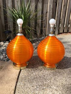 two orange vases sitting next to each other on the ground in front of a fence