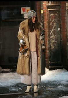 a woman is standing in the snow with her hand on her hip and wearing a fur coat