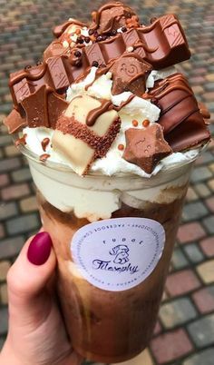 a person holding up a chocolate milkshake with whipped cream and chocolate chunks on top