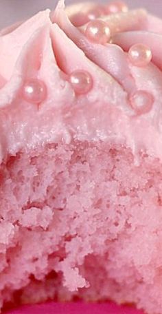 a close up of a pink cake with white frosting and pearls on the top