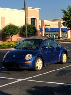 a small blue car parked in a parking lot next to a shopping center and store