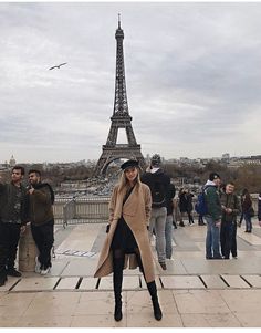 a woman standing in front of the eiffel tower with people walking around her