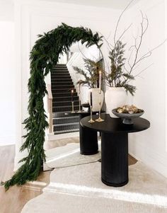 a black table topped with greenery next to a white wall and stair leading up to the second floor