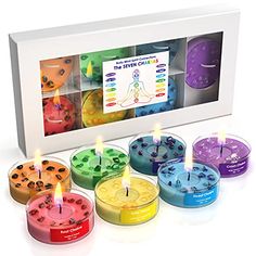 the seven chakra candles are arranged in different colors and sizes, with one lit candle on