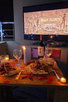 a table set with food and wine in front of a flat screen tv