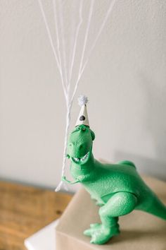 a green toy dinosaur with a party hat and balloons attached to it's head