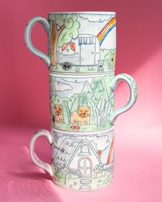 three coffee mugs stacked on top of each other with animals and houses painted on them