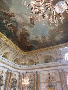 a chandelier hanging from the ceiling in a large room with paintings on it