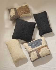 four decorative pillows are arranged on a white sheet with black and brown squares in the middle