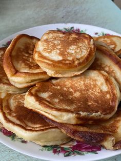 some pancakes are stacked on top of each other in a white and pink plate with floral designs