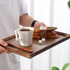 a person holding a tray with bread and coffee