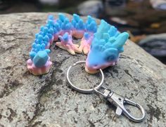 two blue and pink toy animals sitting on top of a rock next to a pair of scissors