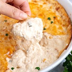 a person dipping some kind of food into a white bowl with parsley on top