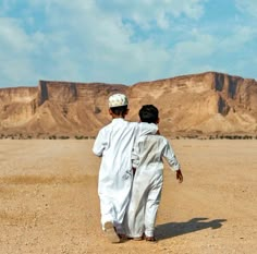 two young boys walking in the desert with mountains in the backgrouds behind them