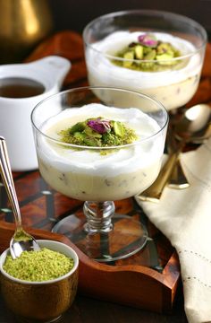 two desserts are sitting on a wooden tray with spoons and cups in front of them