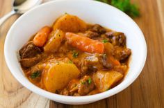 a white bowl filled with stew and carrots on top of a wooden cutting board