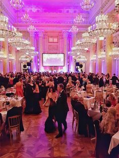 a large ballroom with chandeliers and tables full of people in formal wear dancing