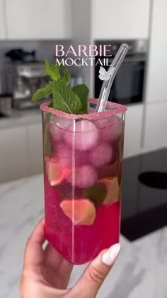 a hand holding a glass filled with pink liquid and green leafy garnish